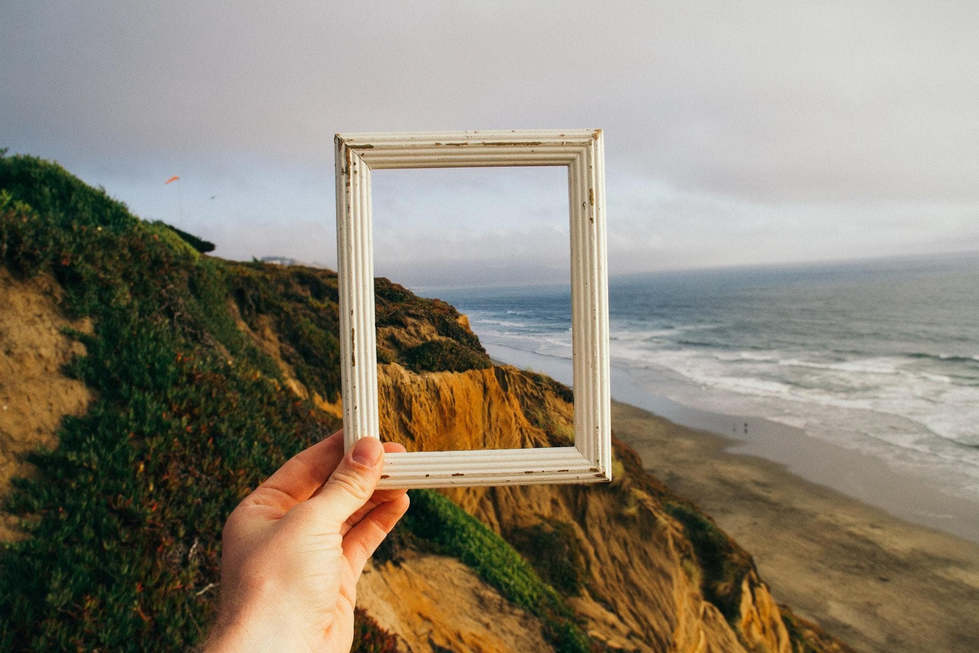 A white picture frame in front of a landscape with a beach.