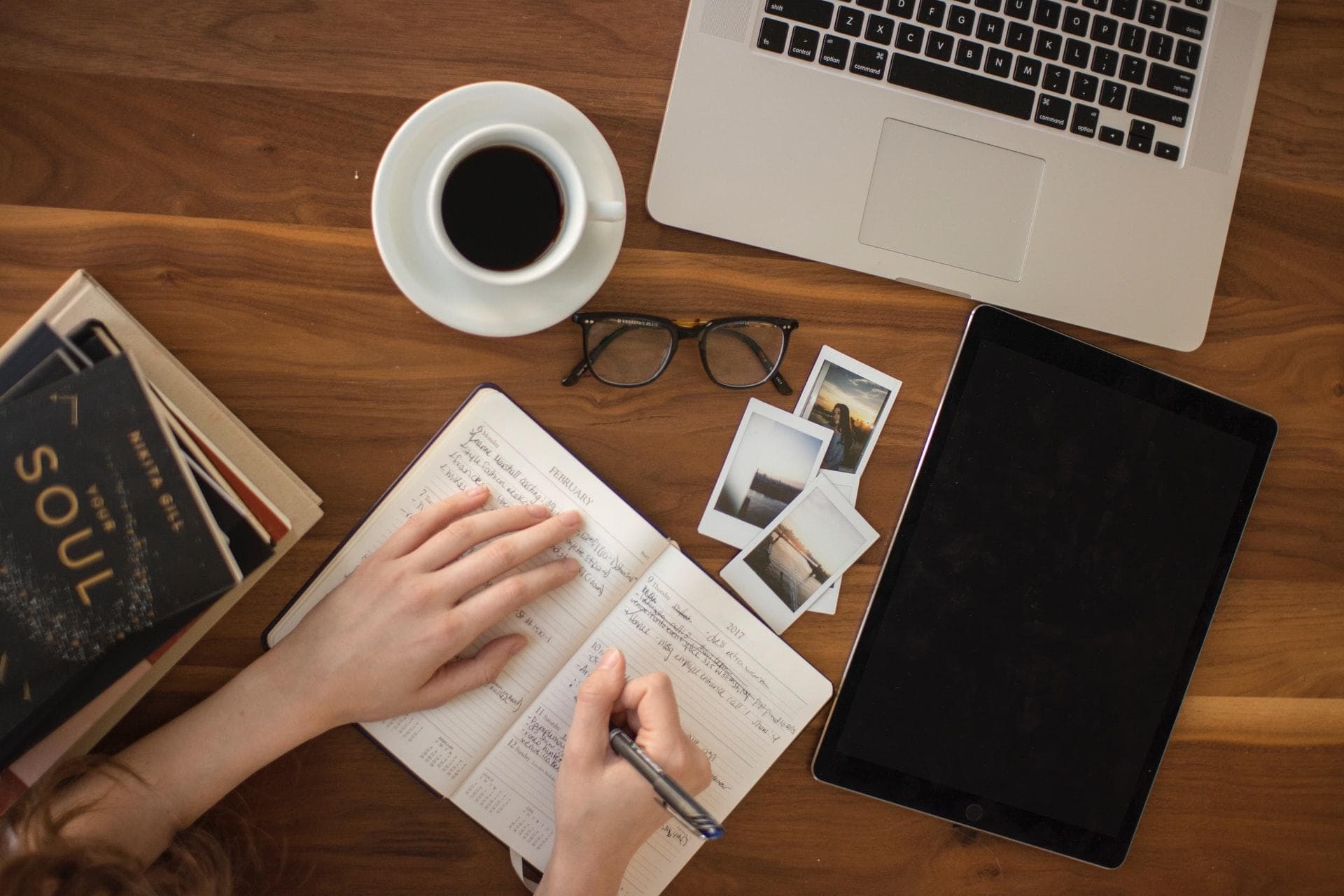 Person writing in a book on a wooden desk.